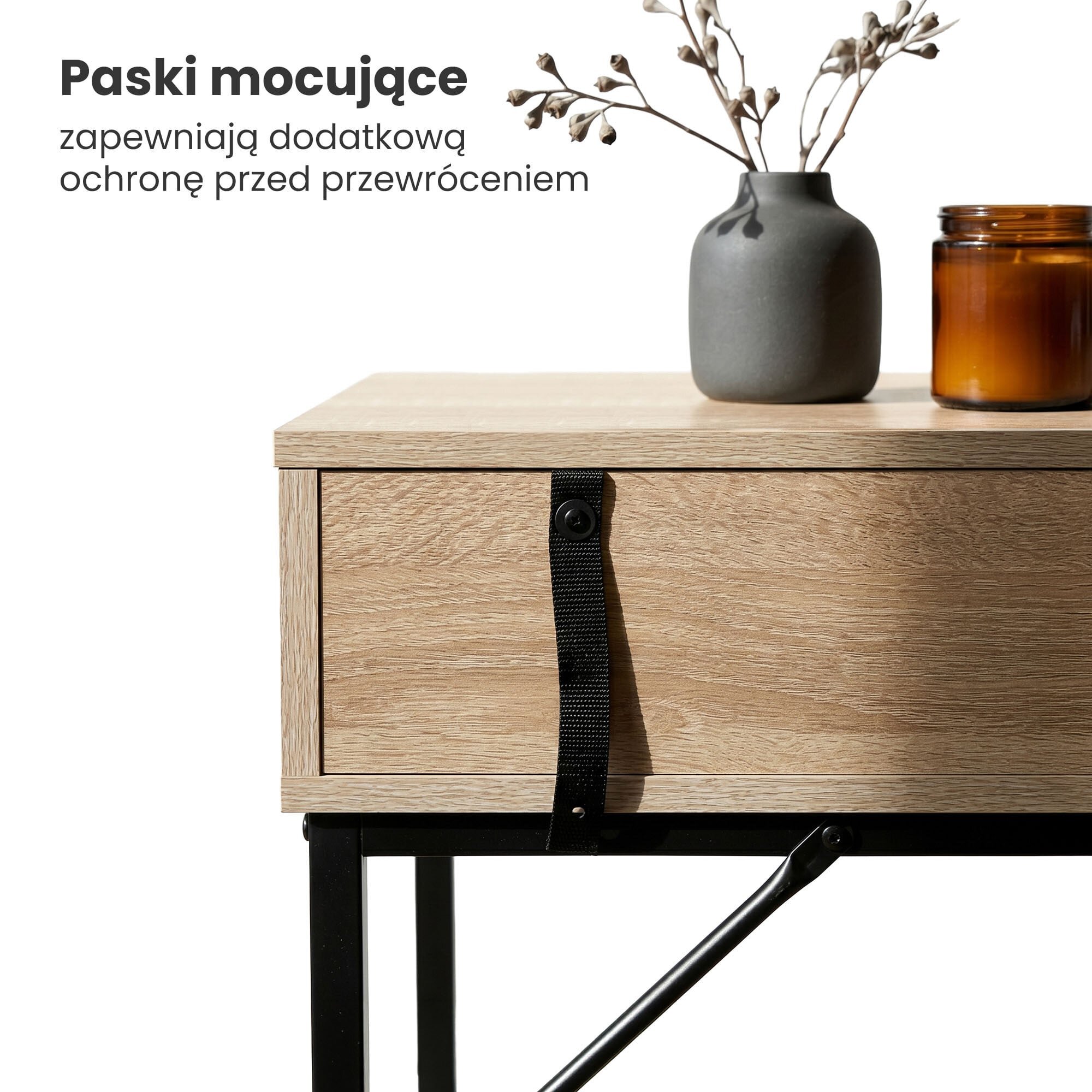 Drewniany stolik z czarnymi metalowymi nogami, na którym stoi szara waza z gałązkami i brązowa świeca. Tekst na obrazie: \'Paski mocujące zapewniają dodatkową ochronę przed przewróceniem\'.