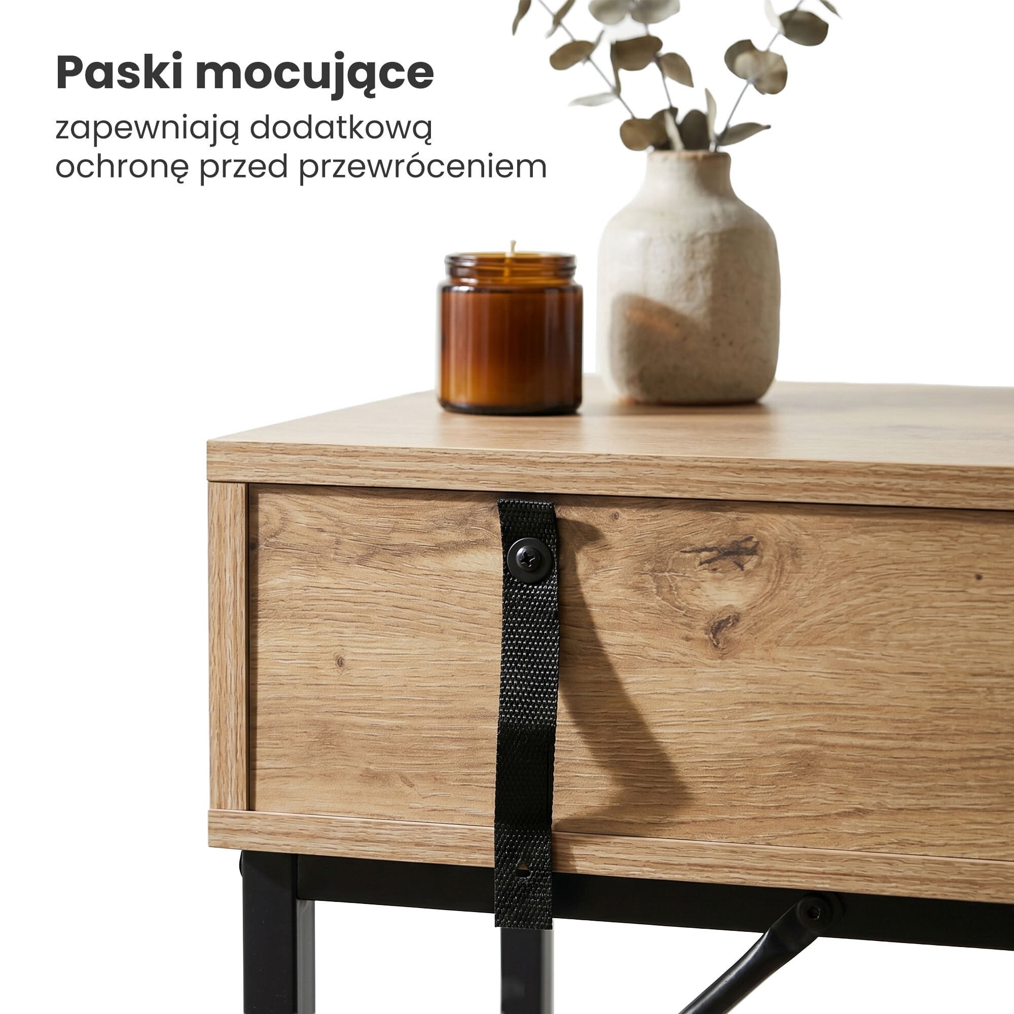 Na zdjęciu widoczny jest fragment drewnianego stolika z czarnymi nogami, na którym stoi brązowa świeca i wazon z rośliną. Obok znajduje się tekst: \'Paski mocujące zapewniają dodatkową ochronę przed przewróceniem\'.
