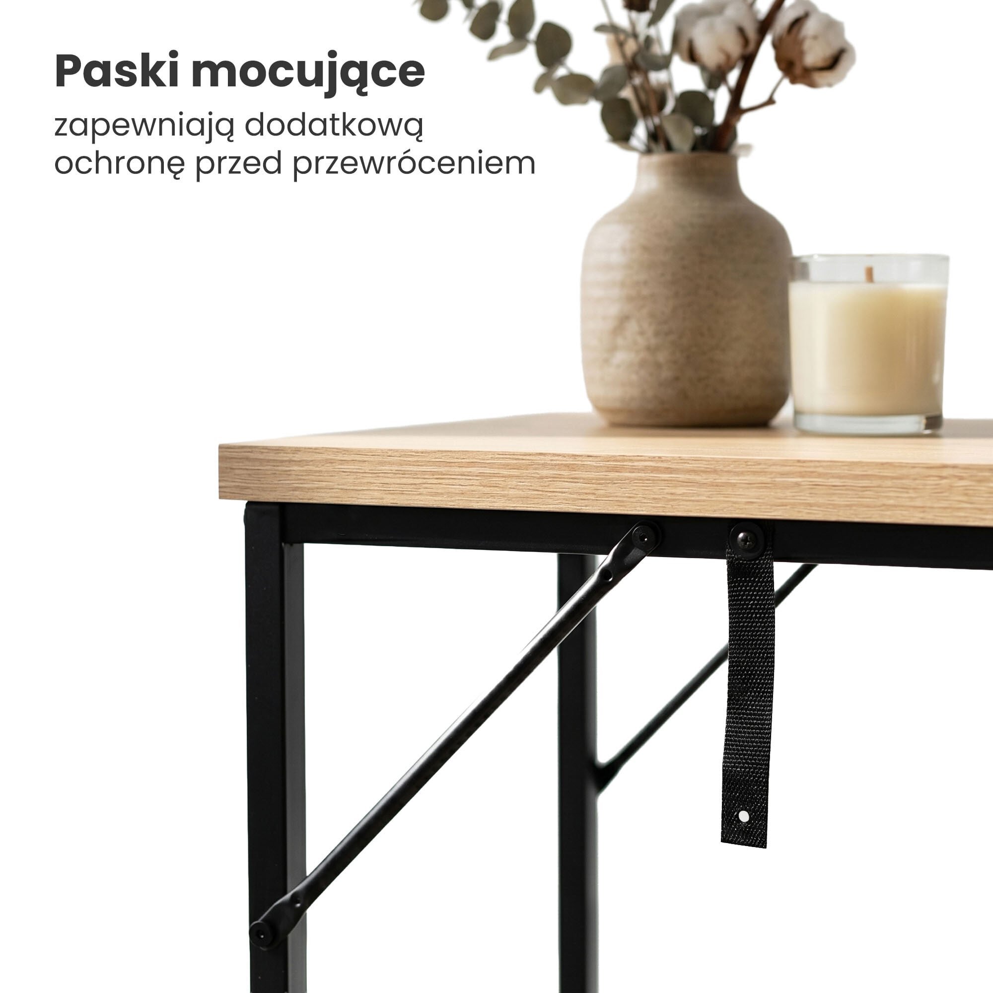 Na zdjęciu widoczny jest fragment stolika z blatem w kolorze dąb sonoma i czarnymi nogami, na którym stoi wazon z roślinami i świeca. Obok znajduje się tekst: \'Paski mocujące zapewniają dodatkową ochronę przed przewróceniem\'.