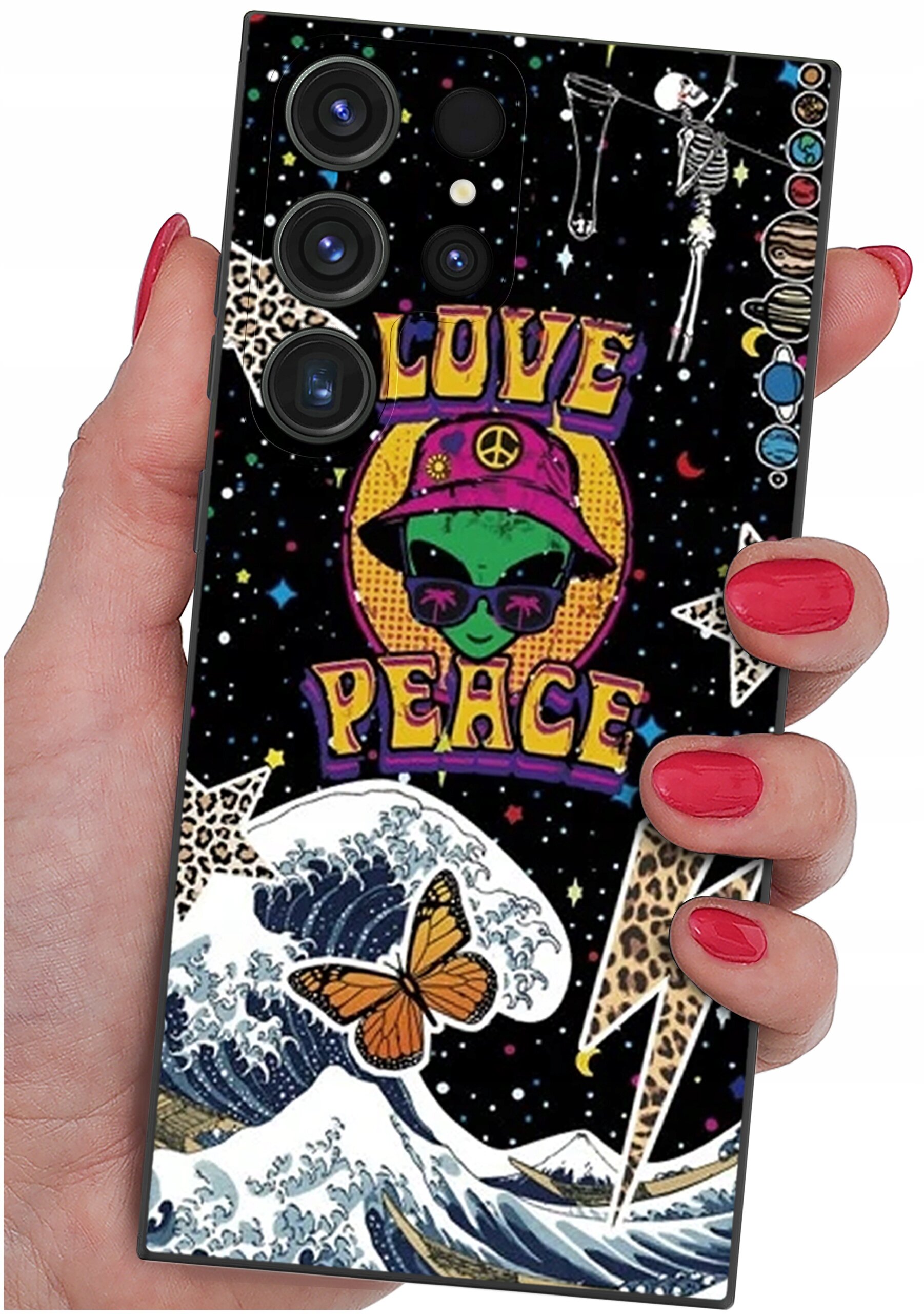 Etui na telefon z kolorowym wzorem przedstawiającym zielonego kosmitę w kapeluszu, napis \'LOVE PEACE\', motyla, fale i szkielety na tle gwiazd. Etui trzymane jest w dłoni z pomalowanymi na czerwono paznokciami.