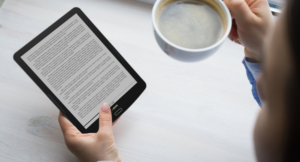 Osoba trzyma czarny czytnik e-booków z wyświetlonym tekstem oraz filiżankę z napojem. Na urządzeniu widoczne jest logo \'inkBOOK\'.
