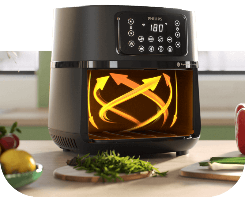 Na obrazie widoczna jest frytkownica beztłuszczowa z wyświetlaczem pokazującym temperaturę 180°C i logo PHILIPS. Wewnątrz urządzenia znajdują się żółte strzałki symbolizujące cyrkulację powietrza, a na blacie obok leżą warzywa i zioła.