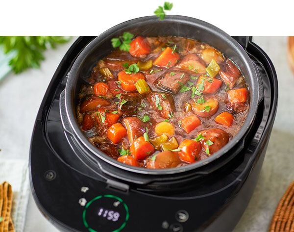 Multicooker z widoczną potrawą z kawałkami mięsa i warzyw. Na wyświetlaczu urządzenia widoczny jest czas 11:59.