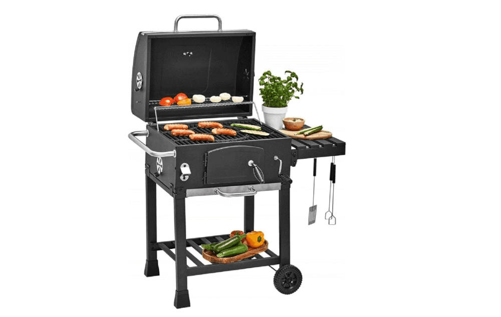 Grill węglowy z otwartą pokrywą, na ruszcie znajdują się różne potrawy, a obok stoi doniczka z ziołami i warzywa. Grill posiada półkę boczną z narzędziami do grillowania oraz dolną półkę z warzywami.