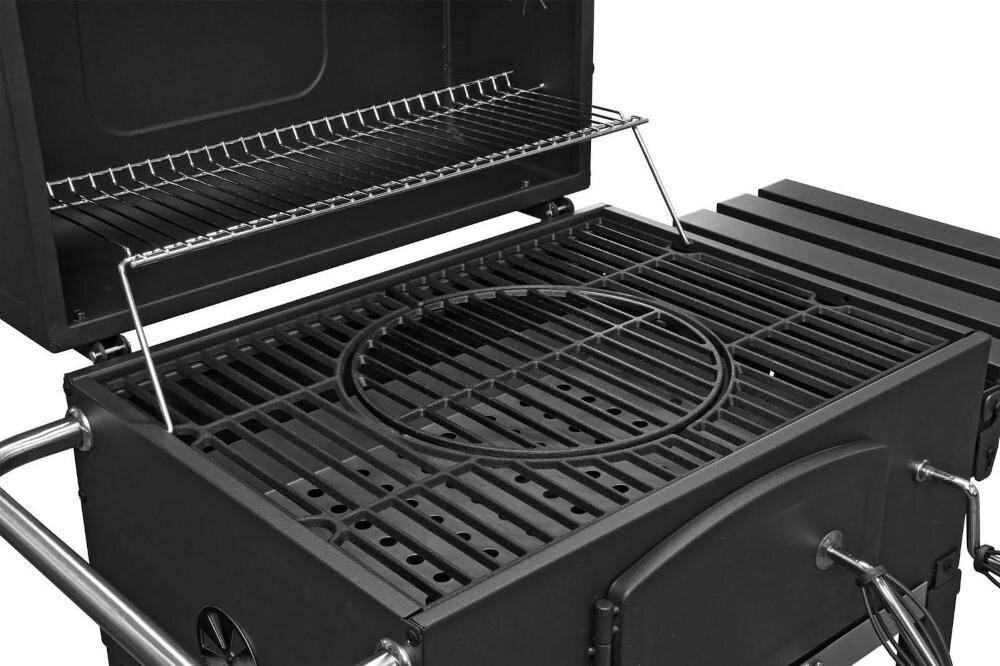 Na obrazie widoczny jest grill węglowy z otwartą pokrywą, posiadający ruszt z okrągłym wycięciem oraz dodatkową półkę na akcesoria. Grill ma solidną konstrukcję z metalowymi elementami i uchwytami.