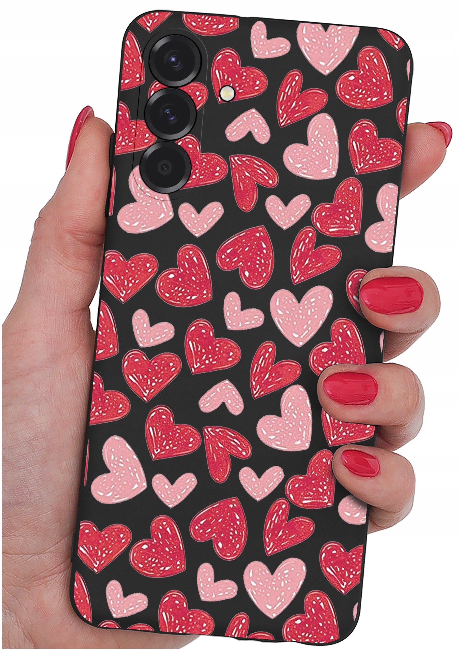 Etui na telefon z wzorem czerwonych i różowych serc trzymane w dłoni z pomalowanymi na czerwono paznokciami. Etui ma trzy otwory na aparaty fotograficzne.