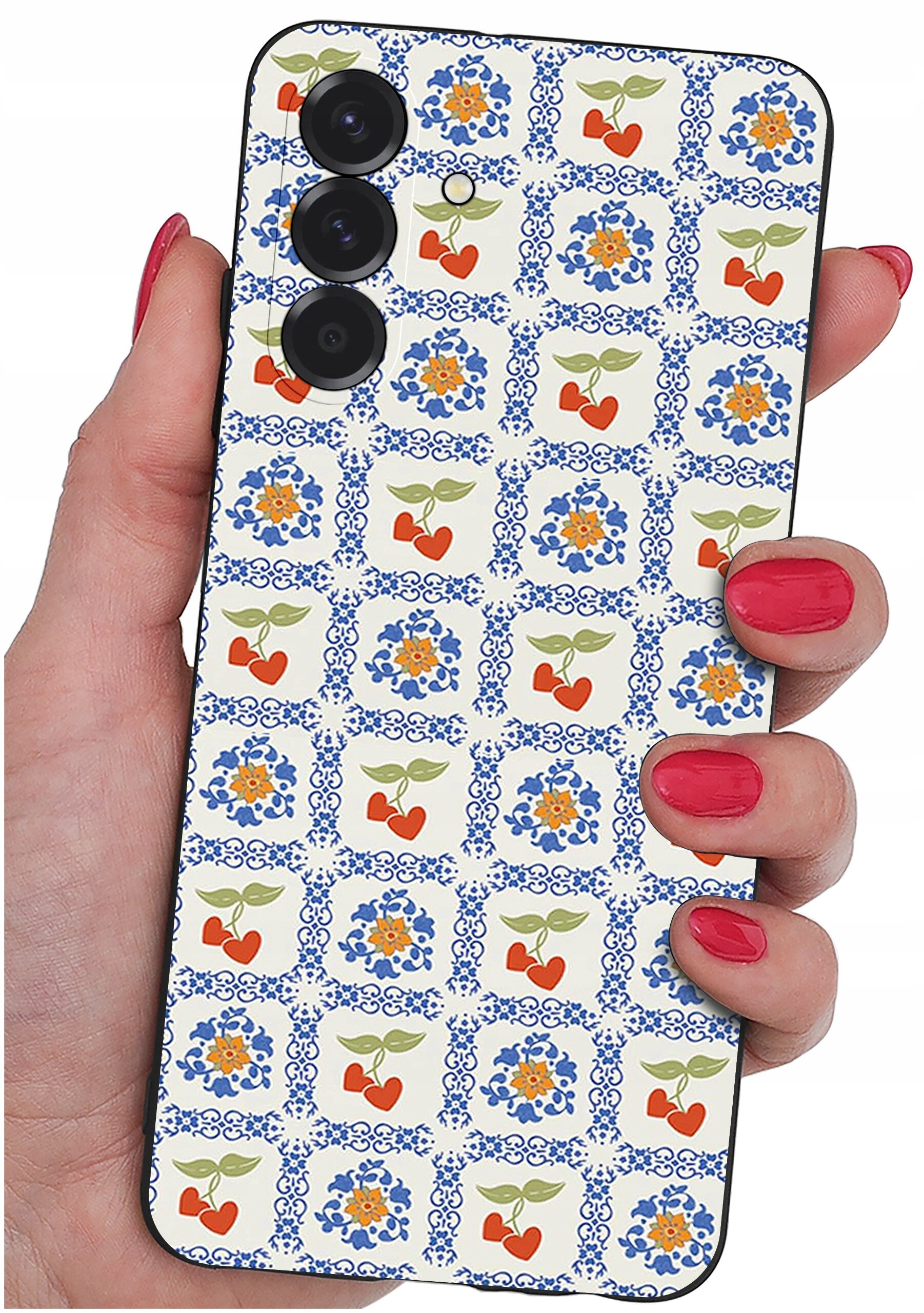 Osoba trzyma telefon z etui ozdobionym wzorem w niebieskie ornamenty i czerwone serca z zielonymi liśćmi. Etui ma trzy otwory na aparaty fotograficzne.