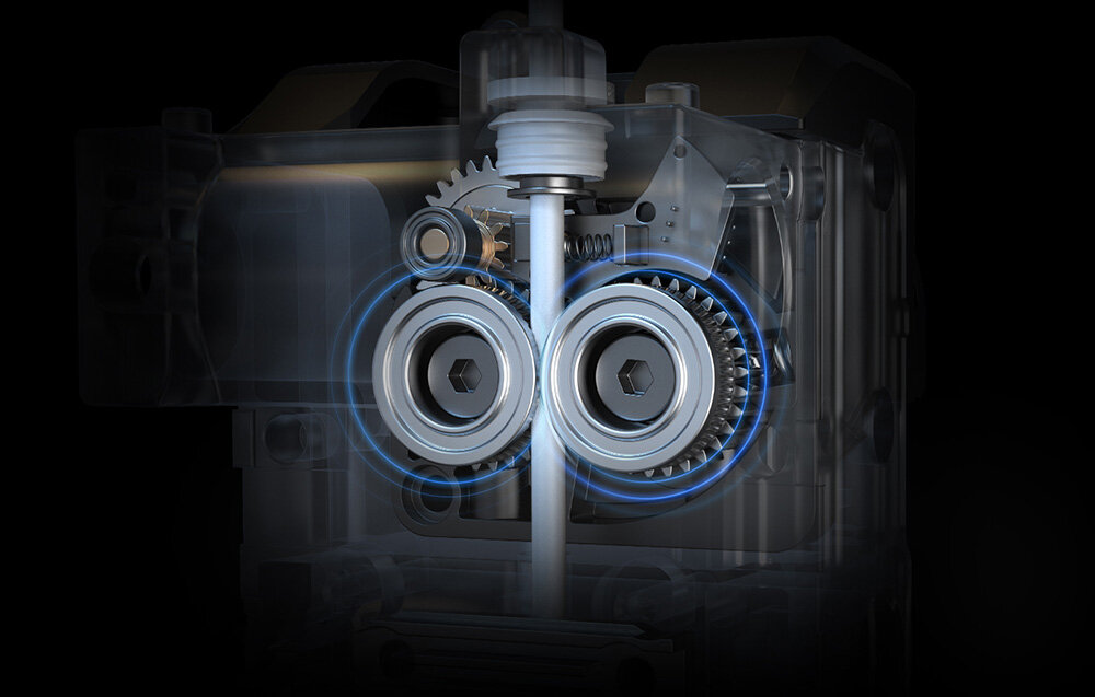 Obraz przedstawia mechanizm z dwoma widocznymi kołami zębatymi i innymi elementami mechanicznymi, otoczony przezroczystą obudową. W tle widoczny jest ciemny, jednolity kolor.