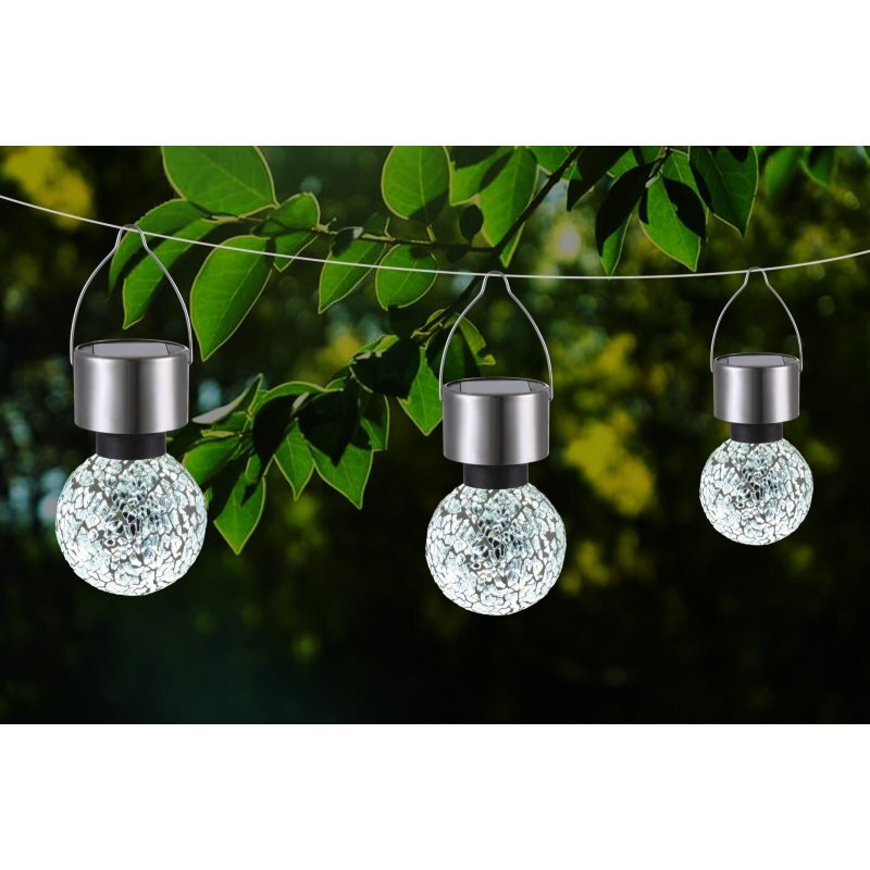 Na obrazie widoczne są trzy wiszące lampki solarne LED o kulistym kształcie z metalowymi uchwytami, zawieszone na tle zielonych liści. Lampki mają dekoracyjną, mozaikową powierzchnię, przez którą przenika światło.