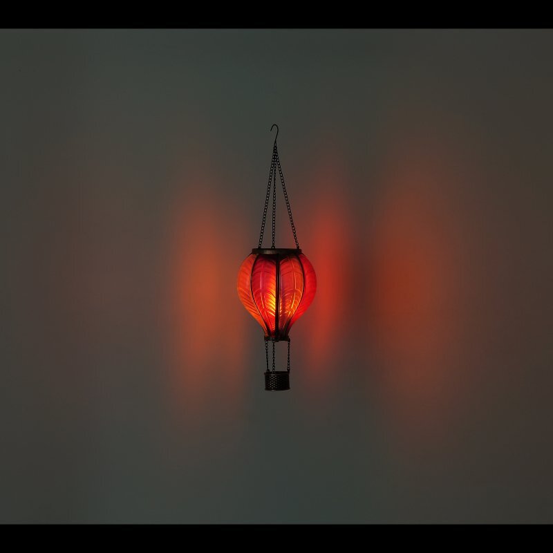 Wisząca lampa solarna w kształcie balonu emituje ciepłe, pomarańczowe światło. Lampa jest zawieszona na łańcuchu i ma dekoracyjny, metalowy uchwyt na dole.