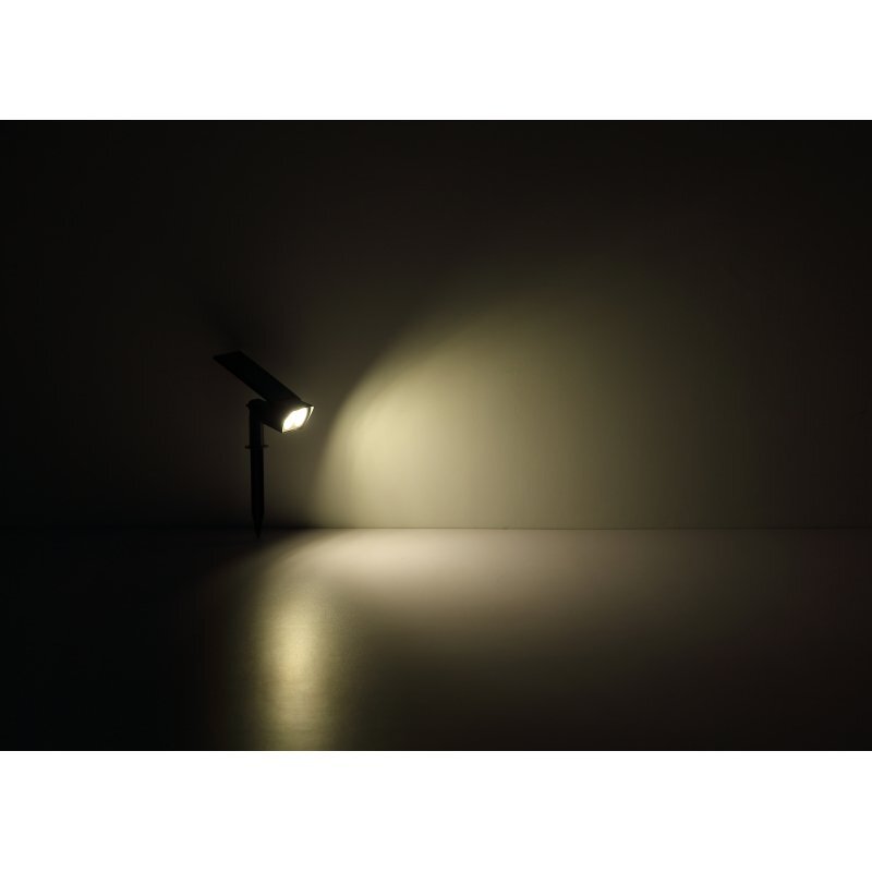 Na obrazie widoczna jest lampa solarna emitująca światło na ciemne tło, tworząc jasną plamę na ścianie i podłodze.