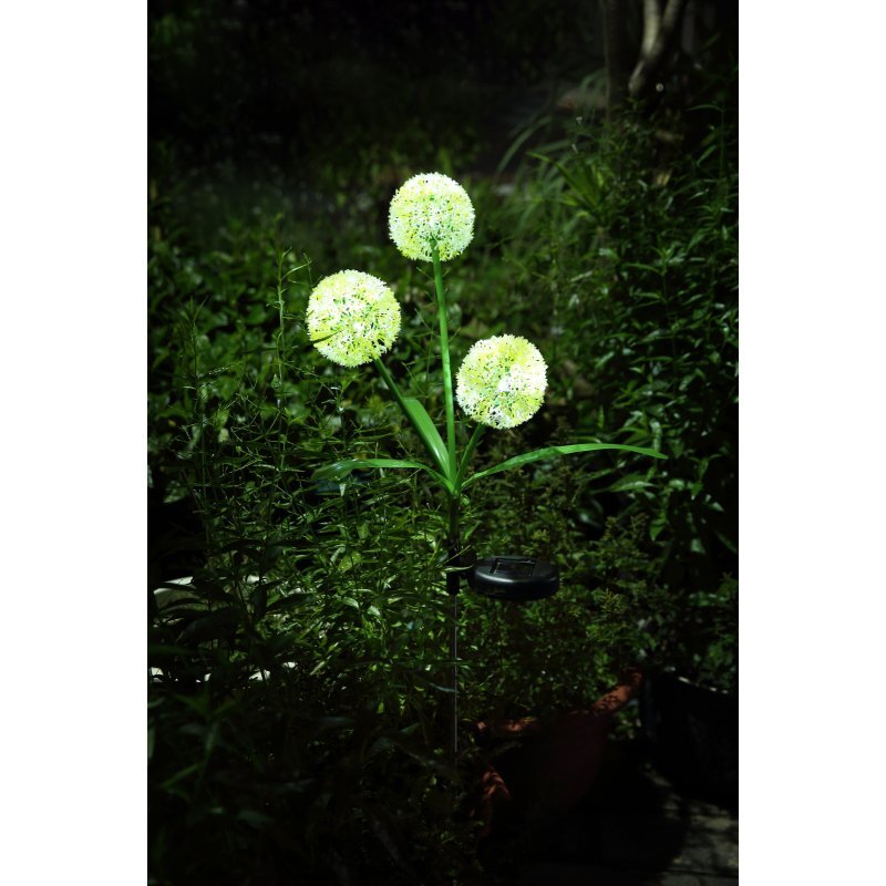 Na obrazie widoczna jest lampa solarna w kształcie trzech kul, świecąca w ciemności, otoczona roślinnością ogrodową. Lampa emituje delikatne, białe światło.