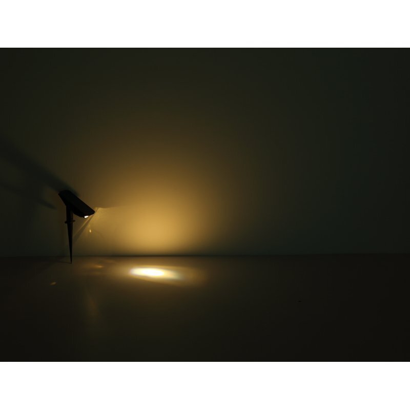 Na ciemnym tle widoczna jest lampa solarna emitująca ciepłe, żółte światło, które oświetla powierzchnię przed nią.