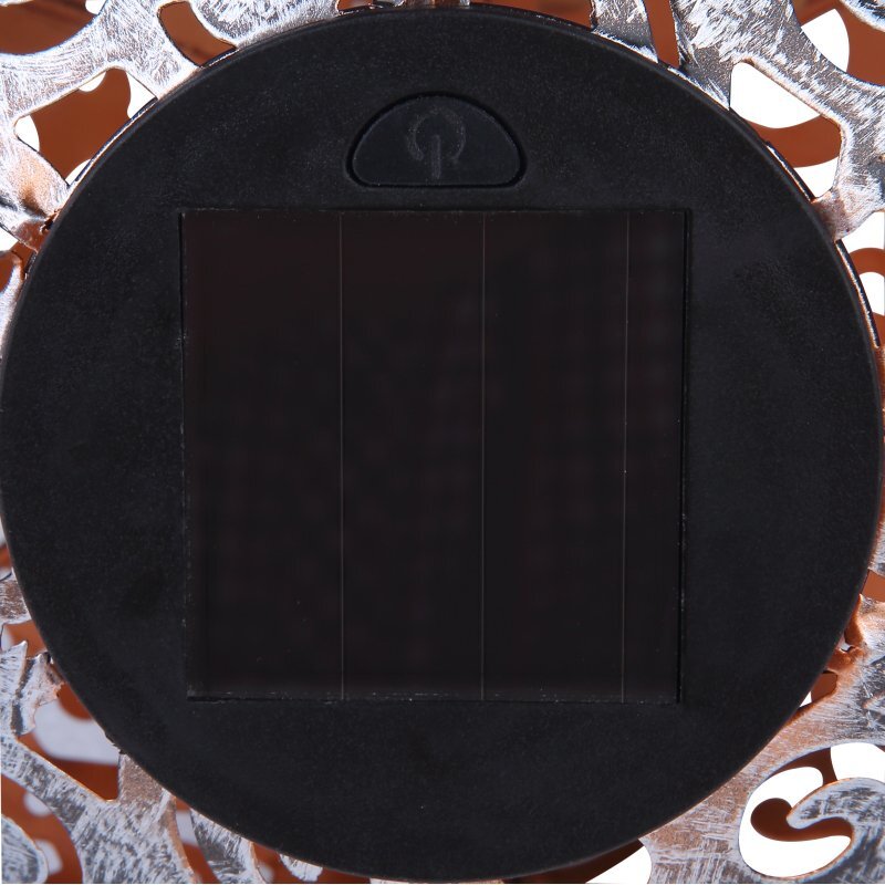 Obraz przedstawia okrągły panel solarny z przyciskiem w kształcie symbolu zasilania na górze. W tle widoczna jest dekoracyjna, ażurowa struktura metalowa.