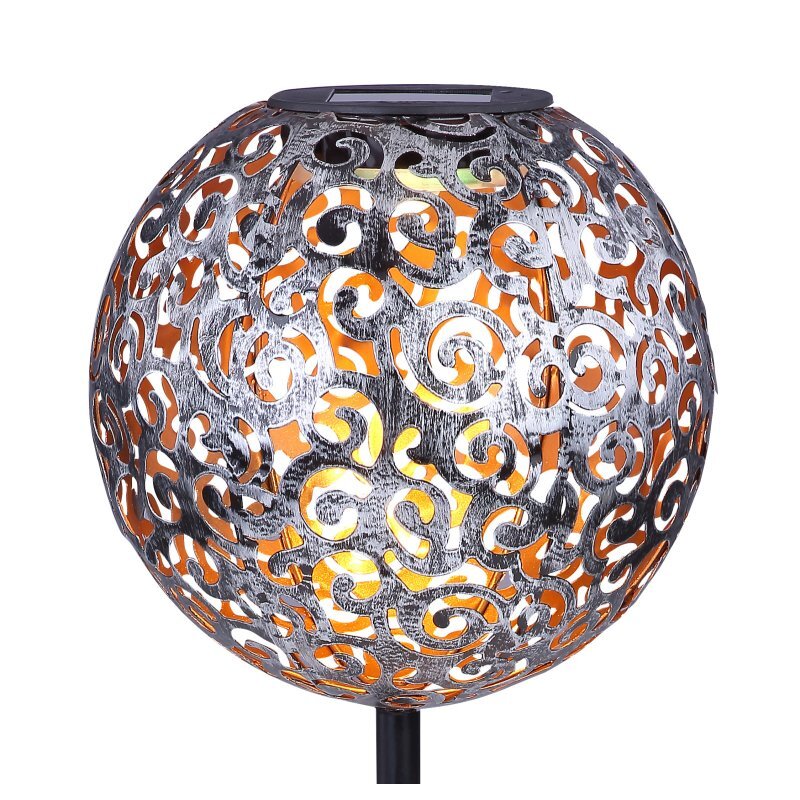 Lampa solarna w kształcie kuli z ażurowym wzorem, przez który prześwituje światło. Wzór składa się z zakrzywionych linii i otworów, a całość jest umieszczona na czarnym pręcie.
