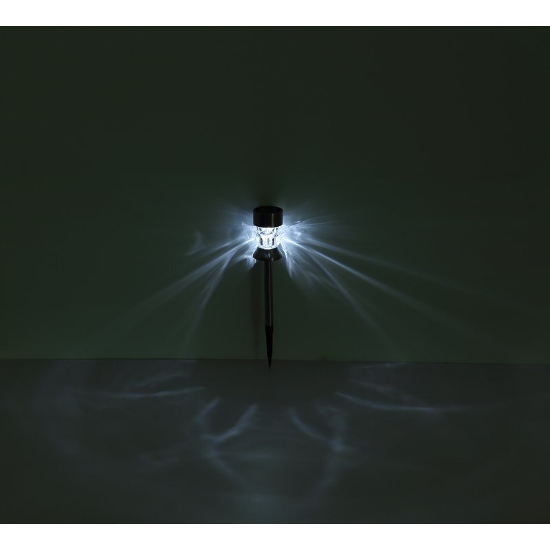 Na ciemnym tle widoczna jest lampa solarna emitująca jasne, rozproszone światło. Lampa ma smukły kształt z ostrym zakończeniem do wbicia w ziemię.