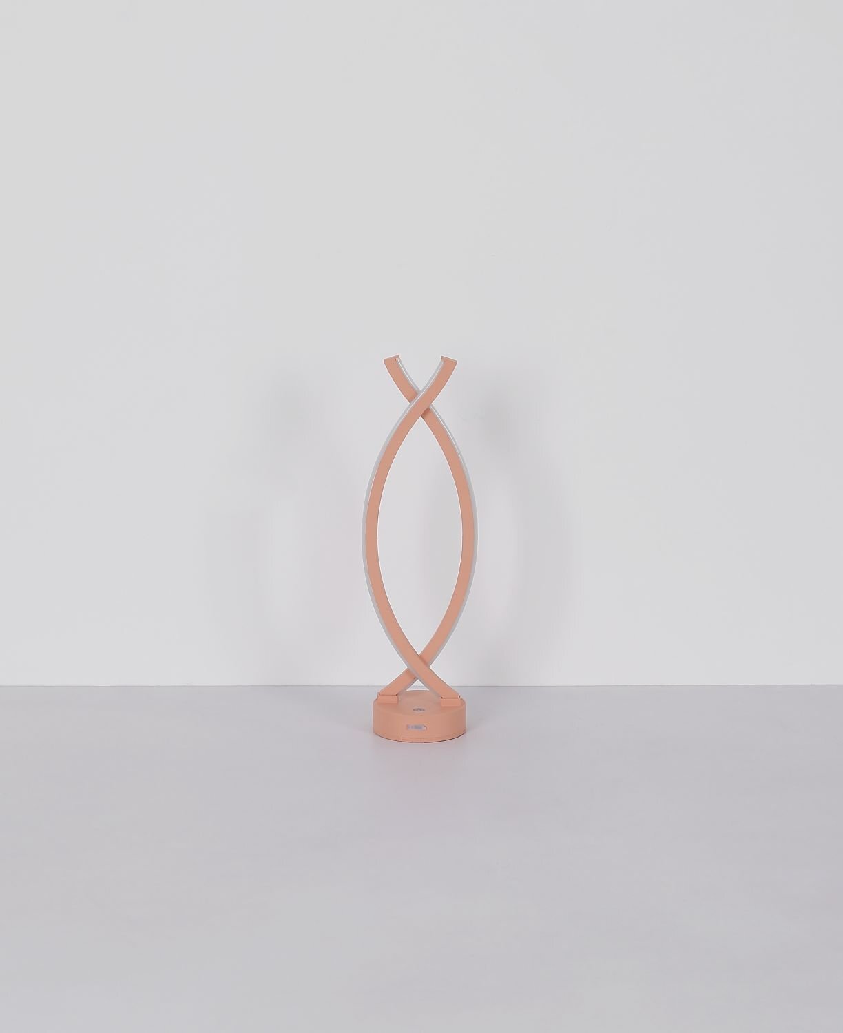 Na obrazie widoczna jest nowoczesna lampa stołowa o spiralnym kształcie w kolorze różowym, umieszczona na jasnym tle. Lampa ma okrągłą podstawę i smukłą, zakrzywioną konstrukcję.