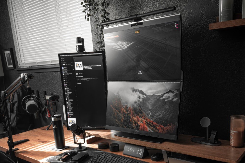 Monitor MOBILE PIXELS Geminos Dual Stanowisko pracy z podwójnym monitorem pionowym na biurku, gdzie górny ekran wyświetla grę, a dolny krajobraz górski, obok drugi monitor w pionie