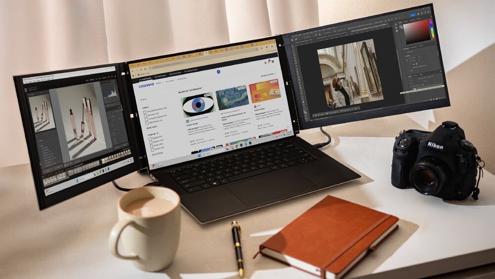 Monitor MOBILE PIXELS Trio 3 Pro Otwarty laptop z doczepionymi dwoma dodatkowymi ekranami po bokach, na których wyświetlane są aplikacje graficzne i strona internetowa Obok stoją aparat, kubek i notes