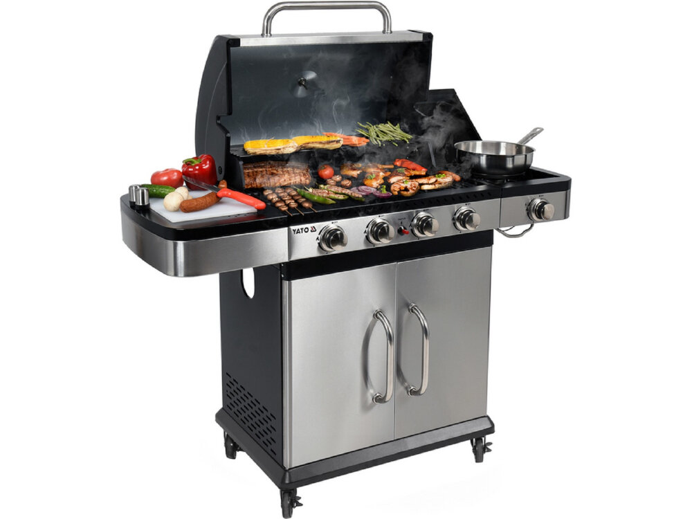 Grill ogrodowy gazowy z otwartą pokrywą, na którym znajdują się różne potrawy, takie jak mięso i warzywa. Na bocznej półce leżą akcesoria kuchenne i warzywa, a na froncie widoczne jest logo \'YATO\'.