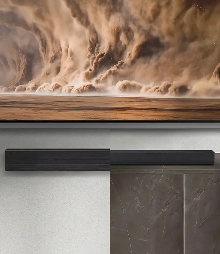 2026-hw-qs90h-top-4-convertible-fit-mo 720x830 Na obrazie widoczny jest soundbar w kolorze grafitowo-czarnym umieszczony pod telewizorem, na którym wyświetlany jest obraz burzy piaskowej. Tło stanowi ściana i szafka w ciemnym kolorze.