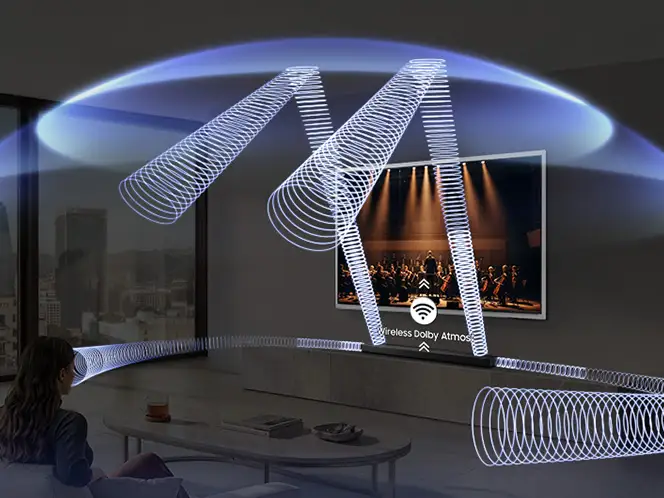 Osoba siedzi w salonie, patrząc na telewizor z wizualizacją dźwięku przestrzennego. Na ekranie widoczny jest napis \'Wireless Dolby Atmos\'.