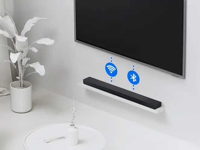 2026-hw-qs90h-wireless-tv-connection 664x498 Na ścianie zamontowany jest czarny soundbar, pod telewizorem. Obok soundbara widoczne są ikony Wi-Fi i Bluetooth.