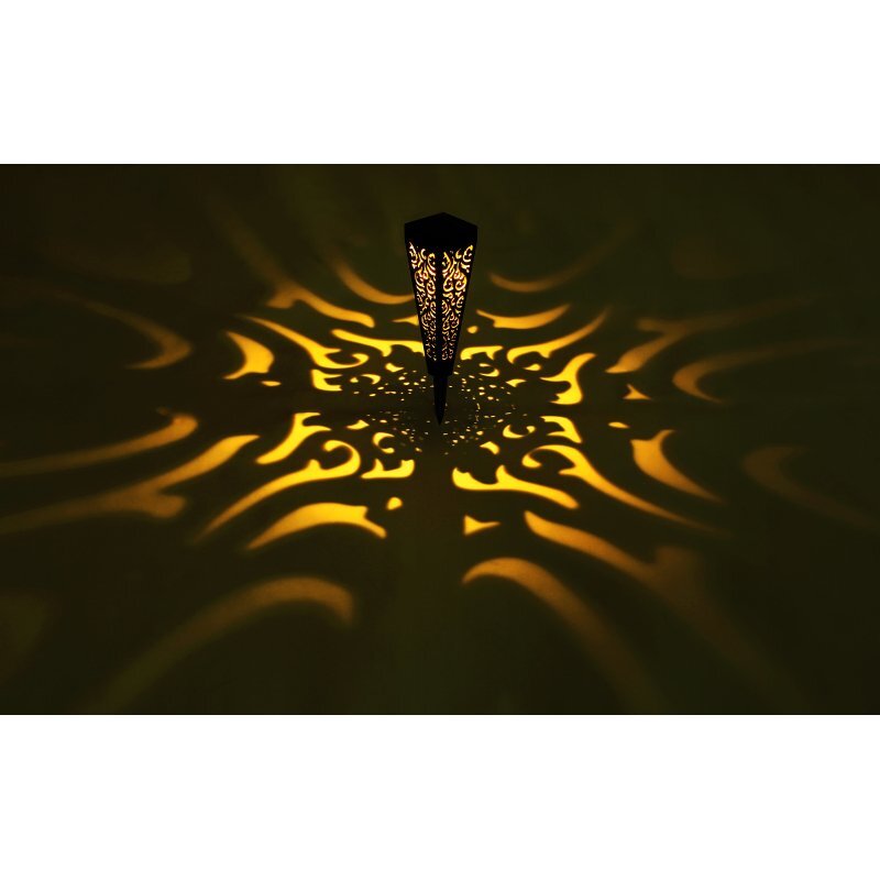 Lampa solarna dogruntowa LED emituje ciepłe, żółte światło, tworząc dekoracyjne wzory na powierzchni wokół niej.