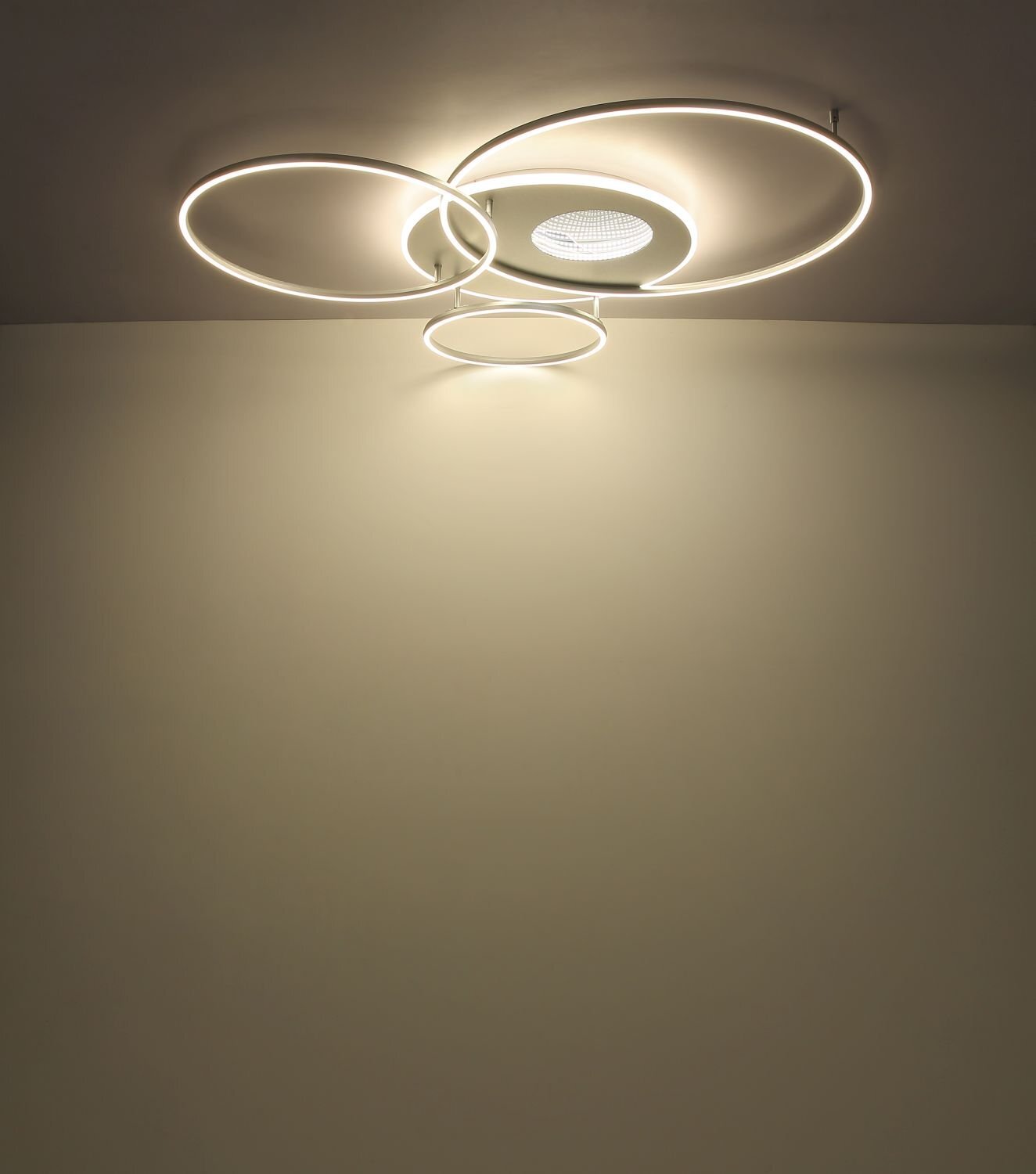 Na suficie zamontowana jest nowoczesna lampa sufitowa LED z trzema okrągłymi pierścieniami emitującymi światło. W centrum znajduje się okrągły element z perforowaną powierzchnią.
