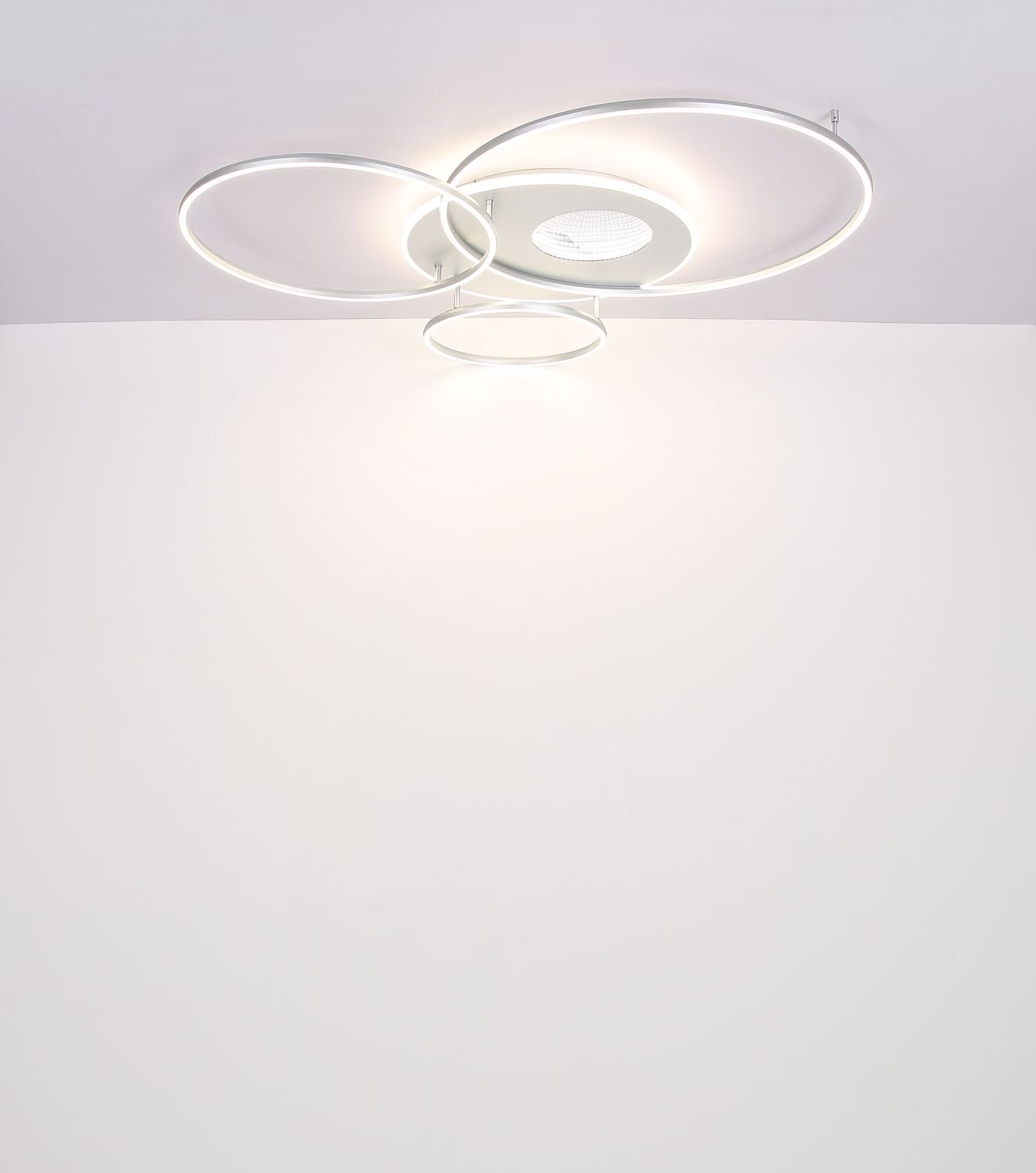 Nowoczesna lampa sufitowa LED z trzema okrągłymi pierścieniami emitującymi światło, zamontowana na suficie. Centralna część lampy jest okrągła i ma kratkowaną powierzchnię.