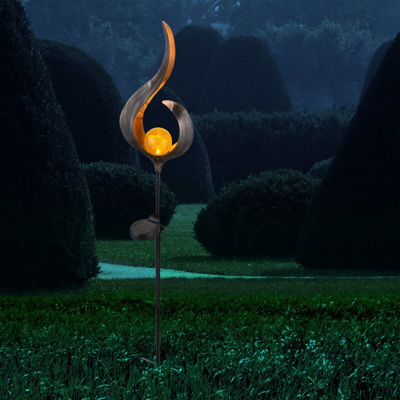 Lampa solarna LED o nowoczesnym designie z kulistym źródłem światła, umieszczona na tle ogrodu w nocy. Światło lampy jest ciepłe i żółte, a otaczają ją ciemne krzewy.