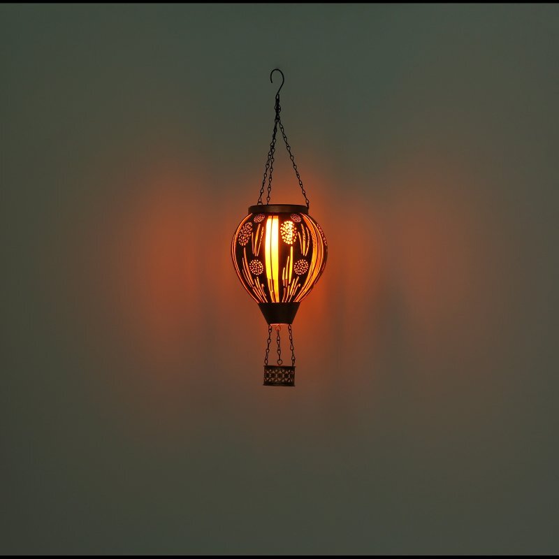 Wisząca lampa w kształcie balonu na ogrzane powietrze, emitująca ciepłe, pomarańczowe światło. Lampa posiada dekoracyjne wzory i jest zawieszona na łańcuszku.