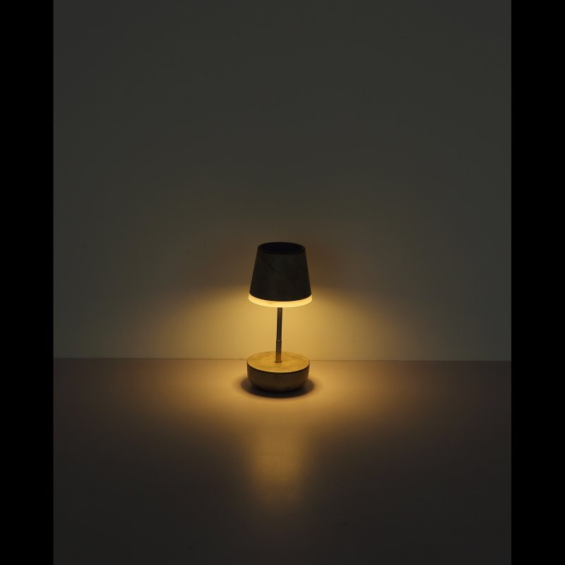 Na obrazie widoczna jest lampa stołowa z ciemnym abażurem, emitująca ciepłe, żółte światło na ciemnym tle.