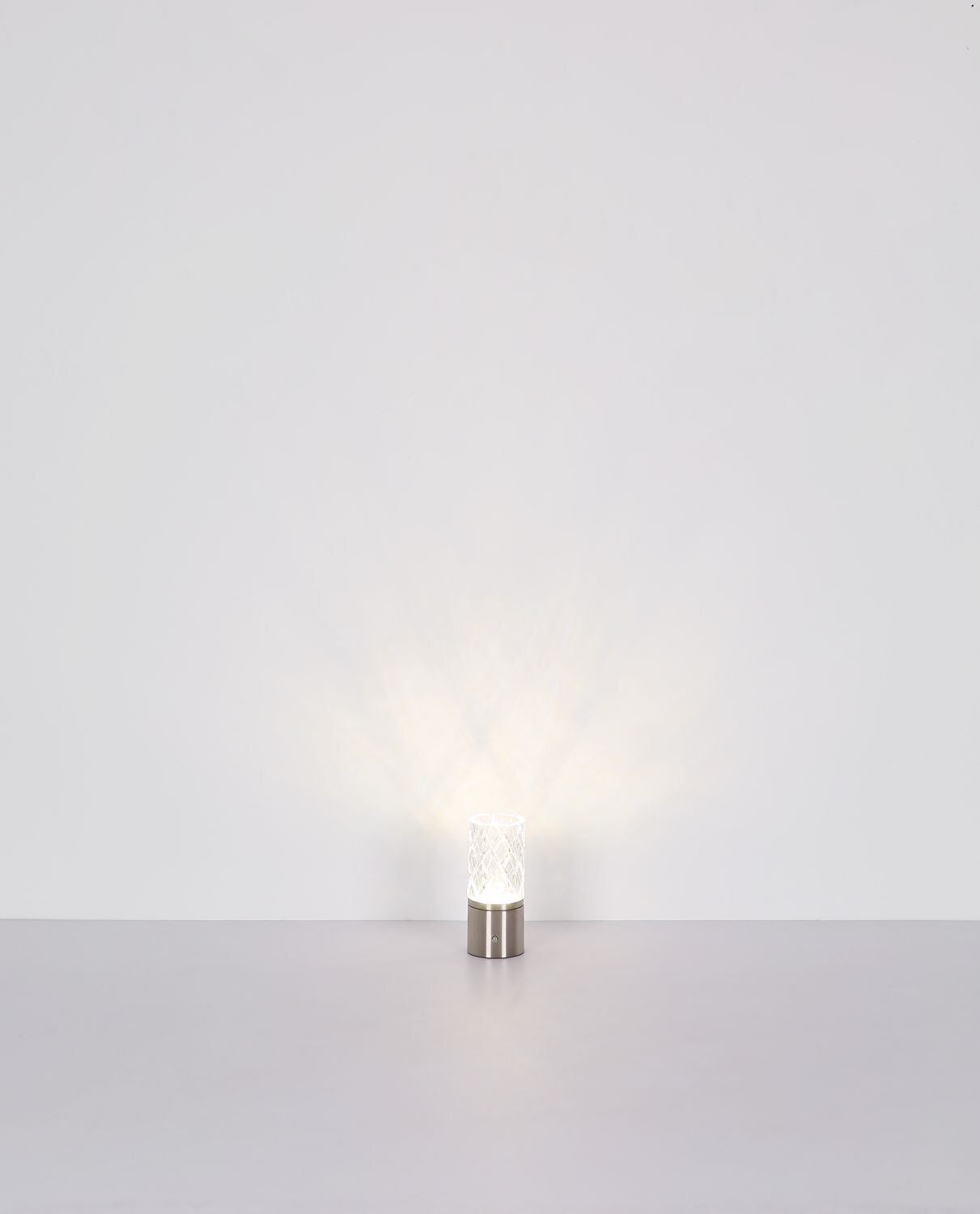 Na obrazie widoczna jest lampa stołowa LED z metalową podstawą i dekoracyjnym kloszem, emitująca delikatne światło. Lampa stoi na gładkiej powierzchni, a tło jest jednolite i jasne.