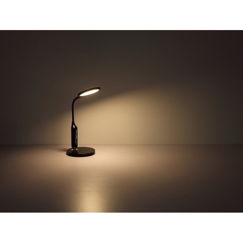 Czarna lampa biurkowa LED z okrągłą podstawą i elastycznym ramieniem, emitująca ciepłe światło na powierzchnię biurka. Lampa posiada dotykowy panel sterowania na podstawie.