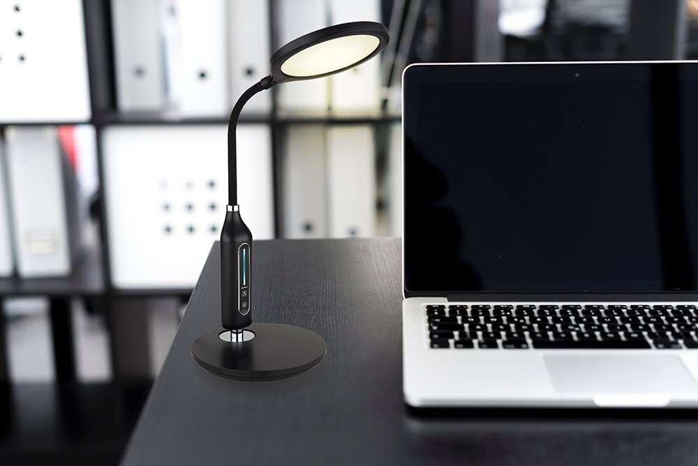 Na biurku znajduje się czarna lampa biurkowa LED z okrągłym kloszem i elastycznym ramieniem, obok laptopa. W tle widoczne są półki z segregatorami.