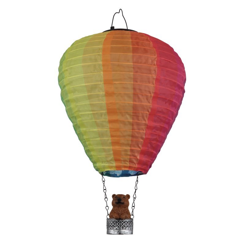 Kolorowy balon w kształcie lampy solarnej z koszem, w którym znajduje się figurka misia. Balon ma pionowe pasy w odcieniach zieleni, pomarańczu i czerwieni.