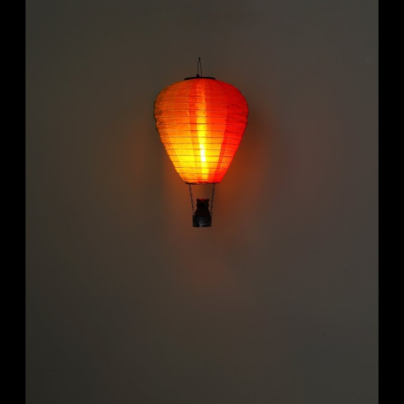 Na obrazie widoczna jest wisząca lampa w kształcie balonu, emitująca ciepłe, pomarańczowe światło. Lampa jest zawieszona na ciemnym tle.