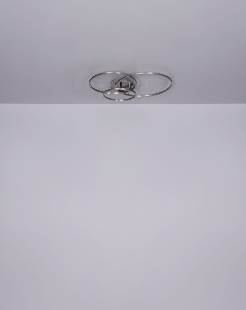 Na suficie zamontowana jest lampa sufitowa z trzema okrągłymi pierścieniami w kolorze satynowym. Tło jest jednolite i jasne.