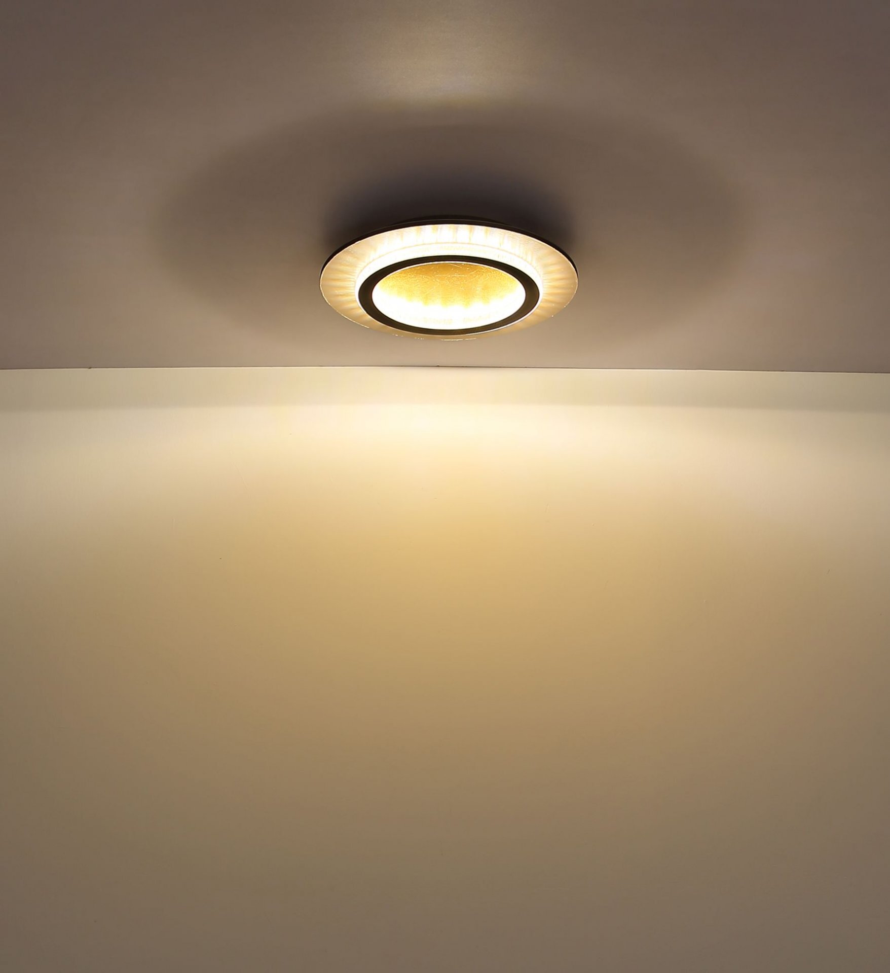 Na suficie zamontowana jest okrągła lampa sufitowa LED, emitująca ciepłe, żółtawe światło. Światło rozchodzi się równomiernie, tworząc delikatny efekt na suficie.