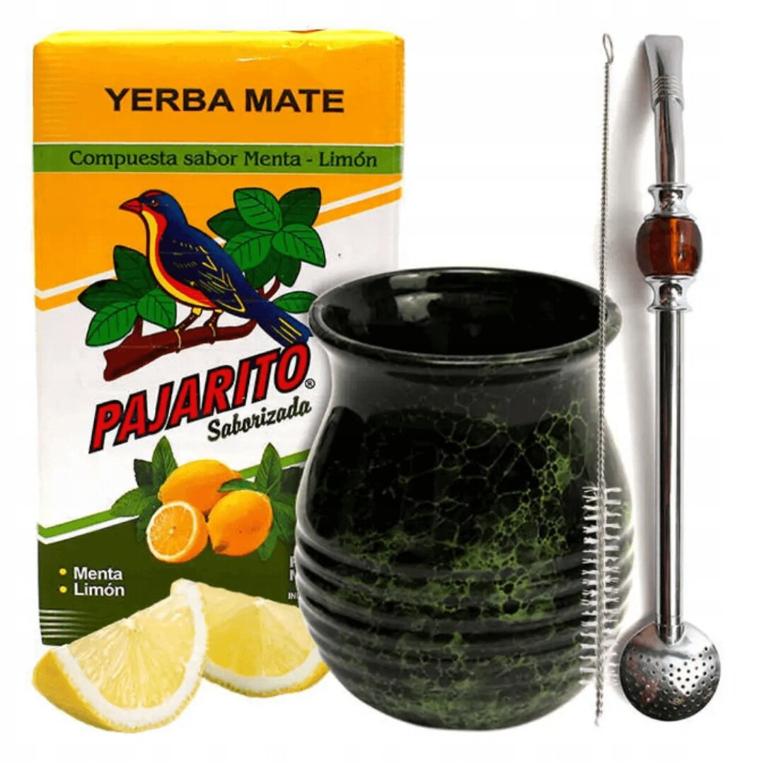 Na obrazie znajduje się opakowanie Yerba Mate Pajarito o smaku mięty i cytryny, czarna tykwa oraz metalowa bombilla z czyścikiem. Obok leżą dwa plasterki cytryny.