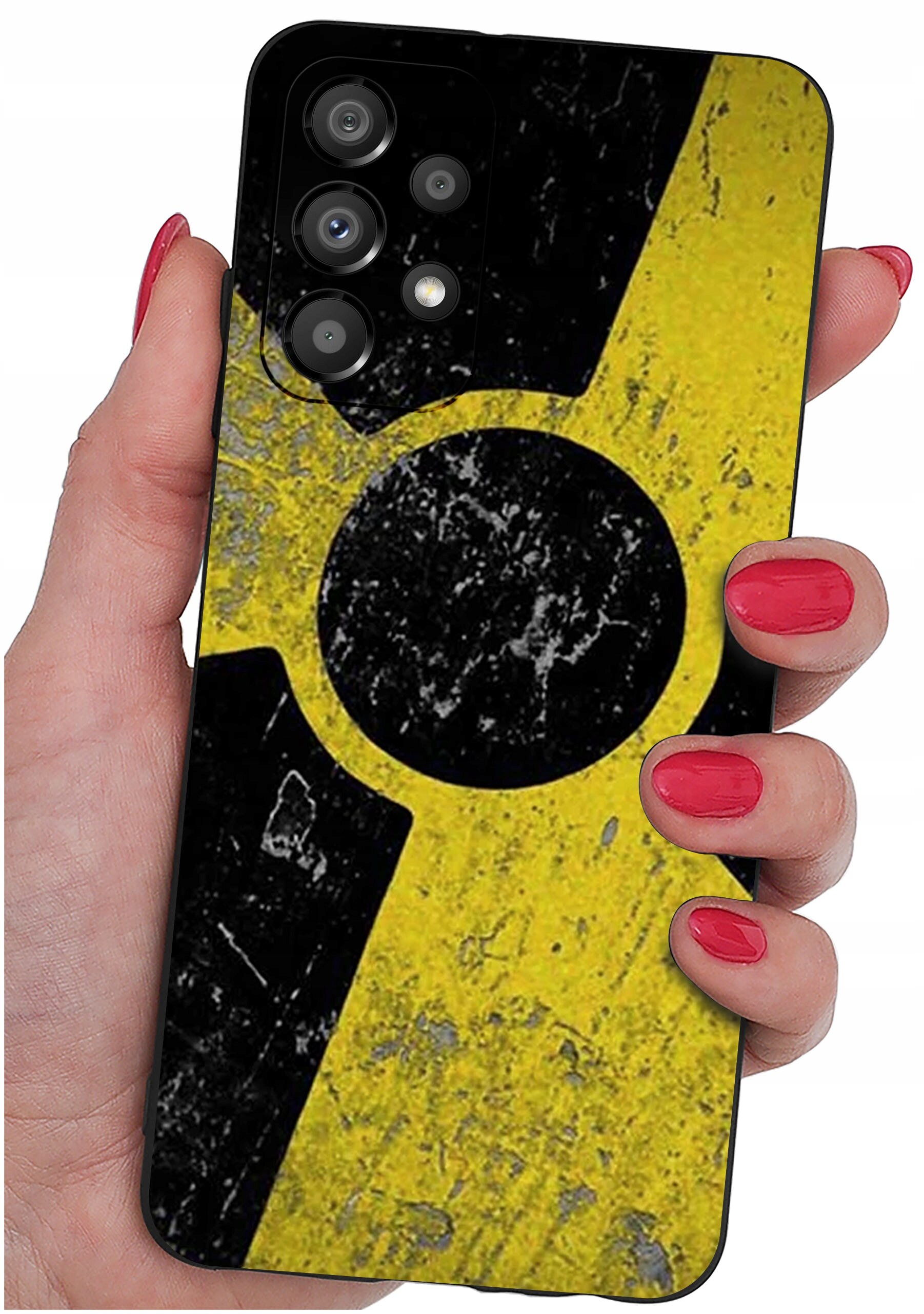 Osoba trzyma telefon z etui o wzorze przypominającym symbol radioaktywności w kolorach żółtym i czarnym. Etui ma matowe wykończenie i widoczne są trzy obiektywy aparatu.