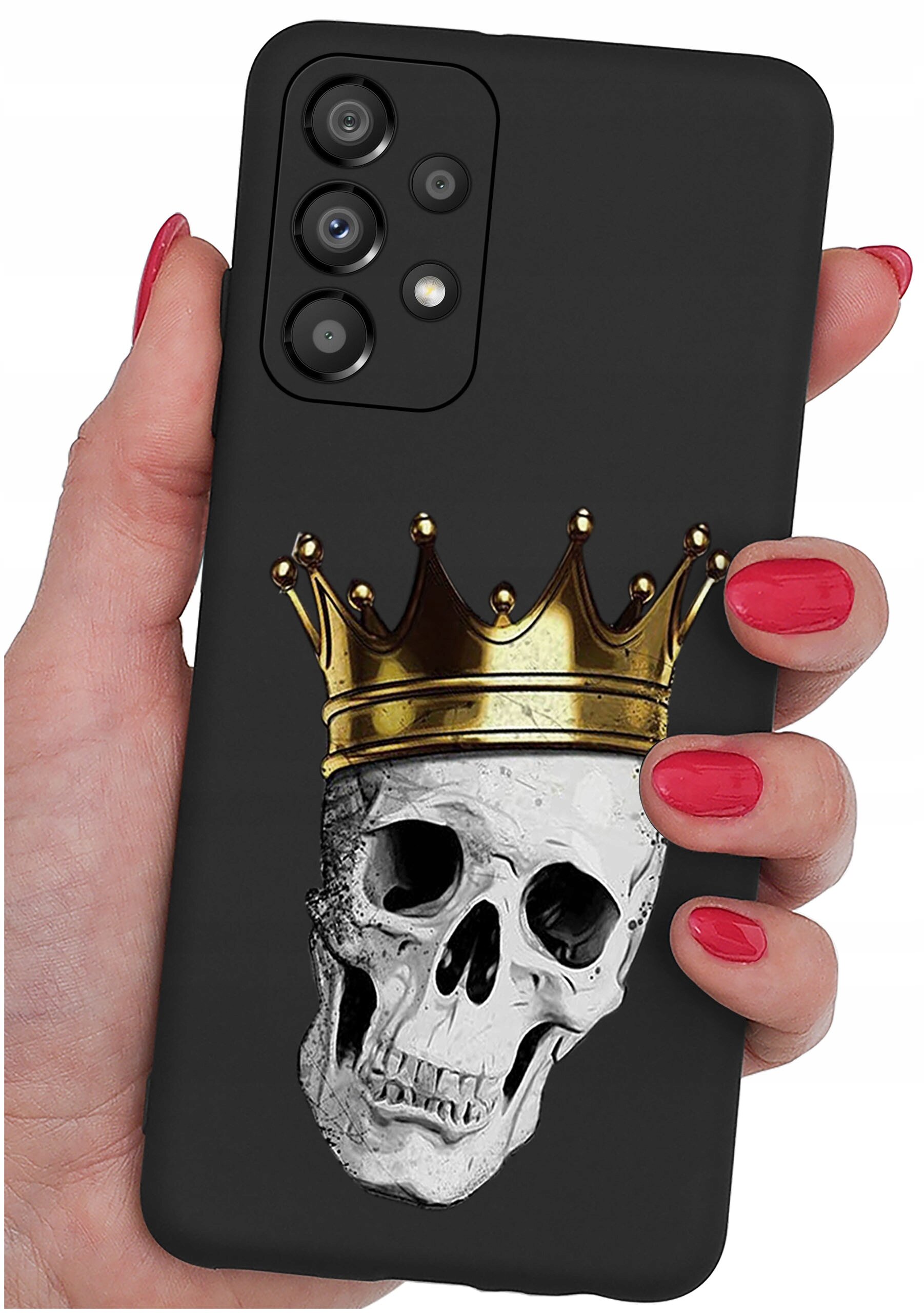 Czarna obudowa telefonu z nadrukiem czaszki w złotej koronie, trzymana w dłoni z czerwonymi paznokciami. Widoczne są cztery obiektywy aparatu na górze obudowy.