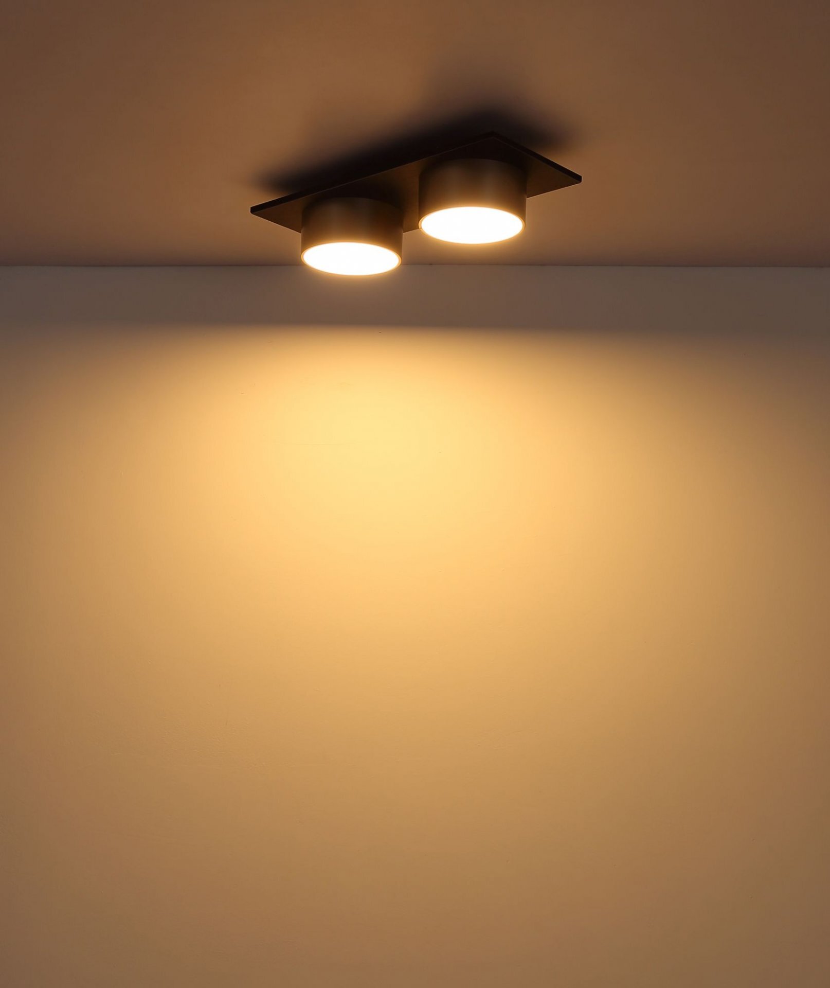Na suficie zamontowana jest nowoczesna lampa sufitowa z dwoma okrągłymi źródłami światła, emitująca ciepłe, żółtawe światło.