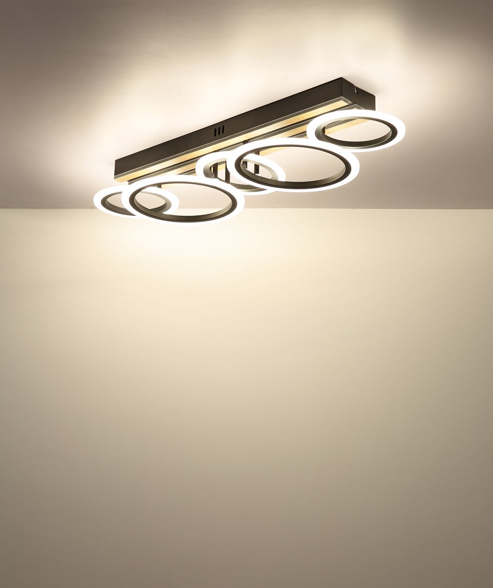 Nowoczesna lampa sufitowa LED z kilkoma okrągłymi elementami świetlnymi, zamontowana na prostokątnej podstawie. Światło jest ciepłe i równomiernie rozproszone na suficie.