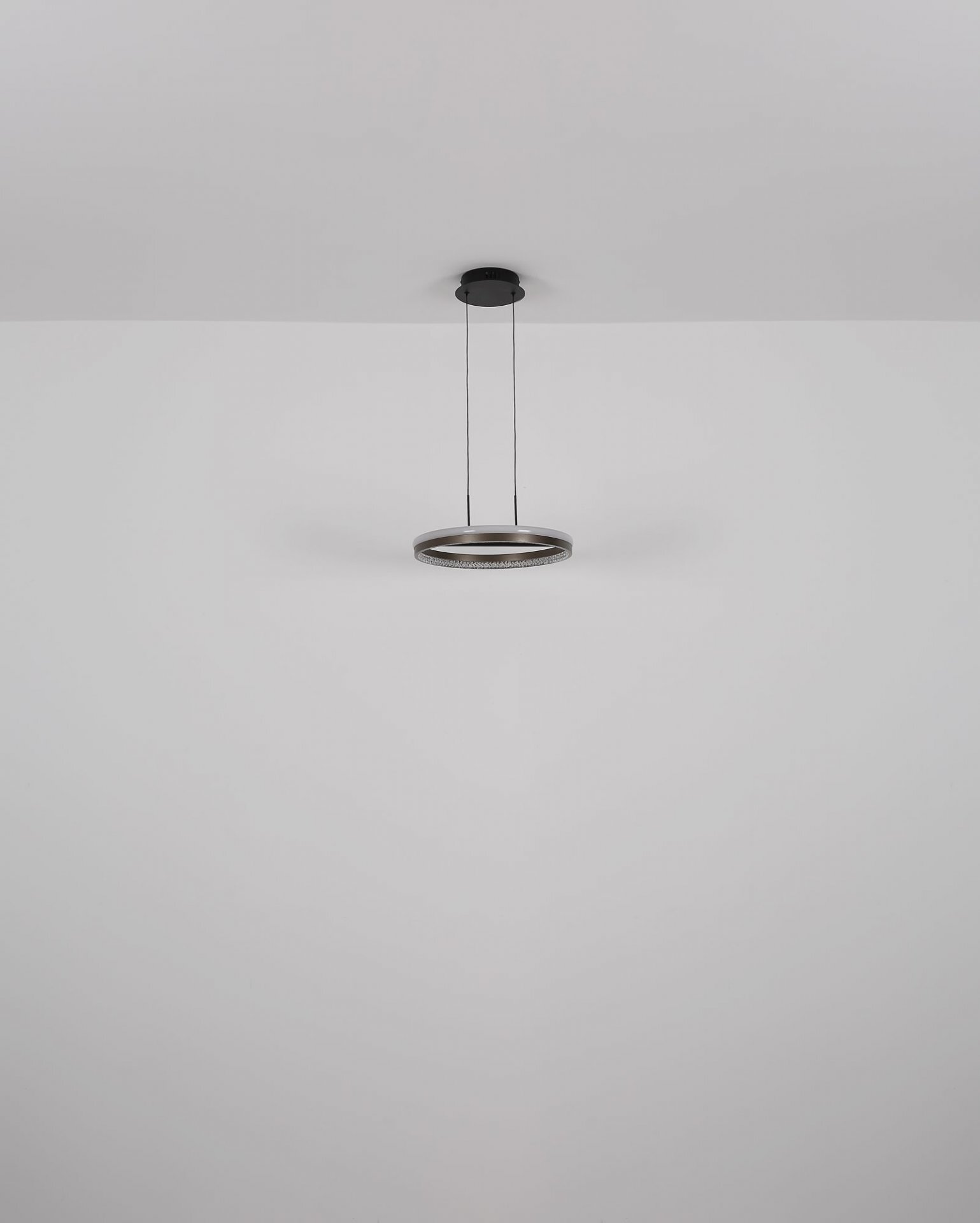 Na obrazie widoczna jest nowoczesna lampa sufitowa o okrągłym kształcie, zawieszona na dwóch cienkich przewodach. Lampa ma metaliczny kolor i jest zamontowana na białym suficie.