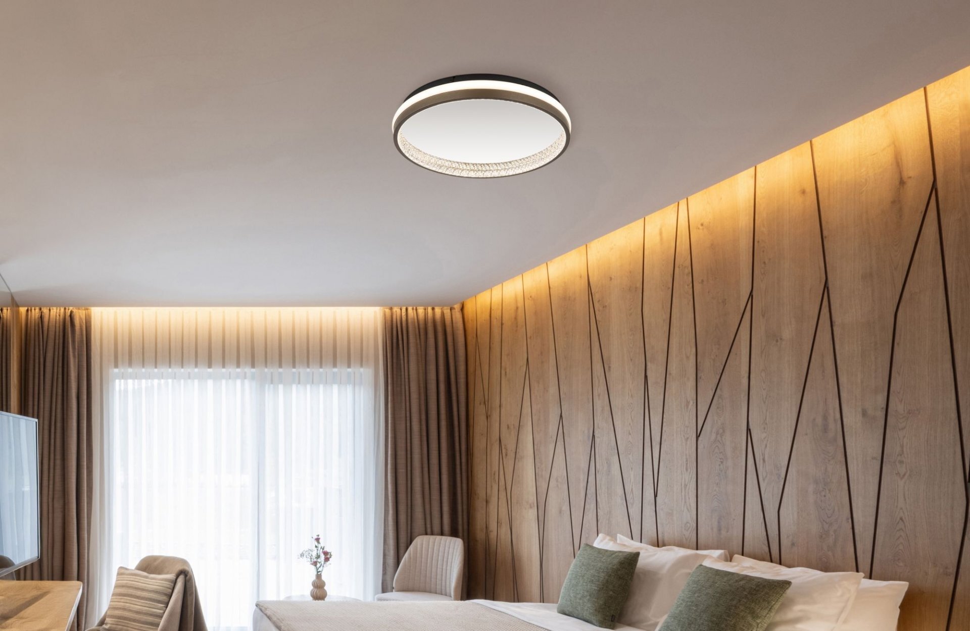 Nowoczesna lampa sufitowa LED zamontowana na suficie w elegancko urządzonym pokoju z drewnianymi panelami na ścianie. W pomieszczeniu znajdują się zasłony, łóżko z poduszkami i krzesło.