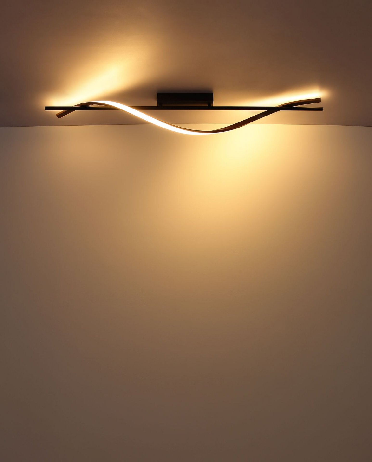 Nowoczesna lampa sufitowa LED z falistym wzorem emitująca ciepłe, żółte światło. Lampa jest zamontowana na suficie i oświetla ścianę poniżej.