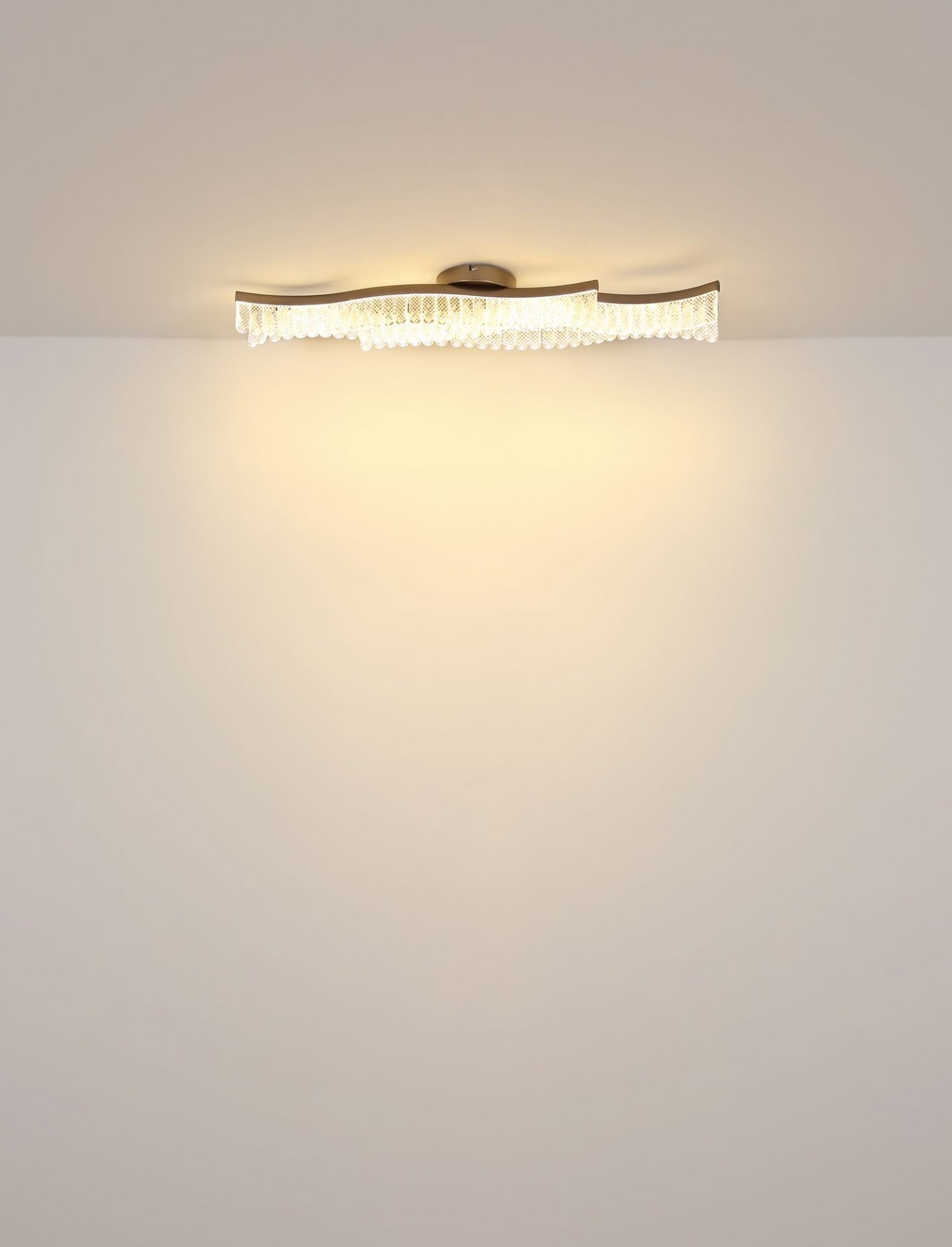 Na obrazie widoczna jest nowoczesna lampa sufitowa LED o falistym kształcie, emitująca ciepłe, rozproszone światło na sufit i ścianę.