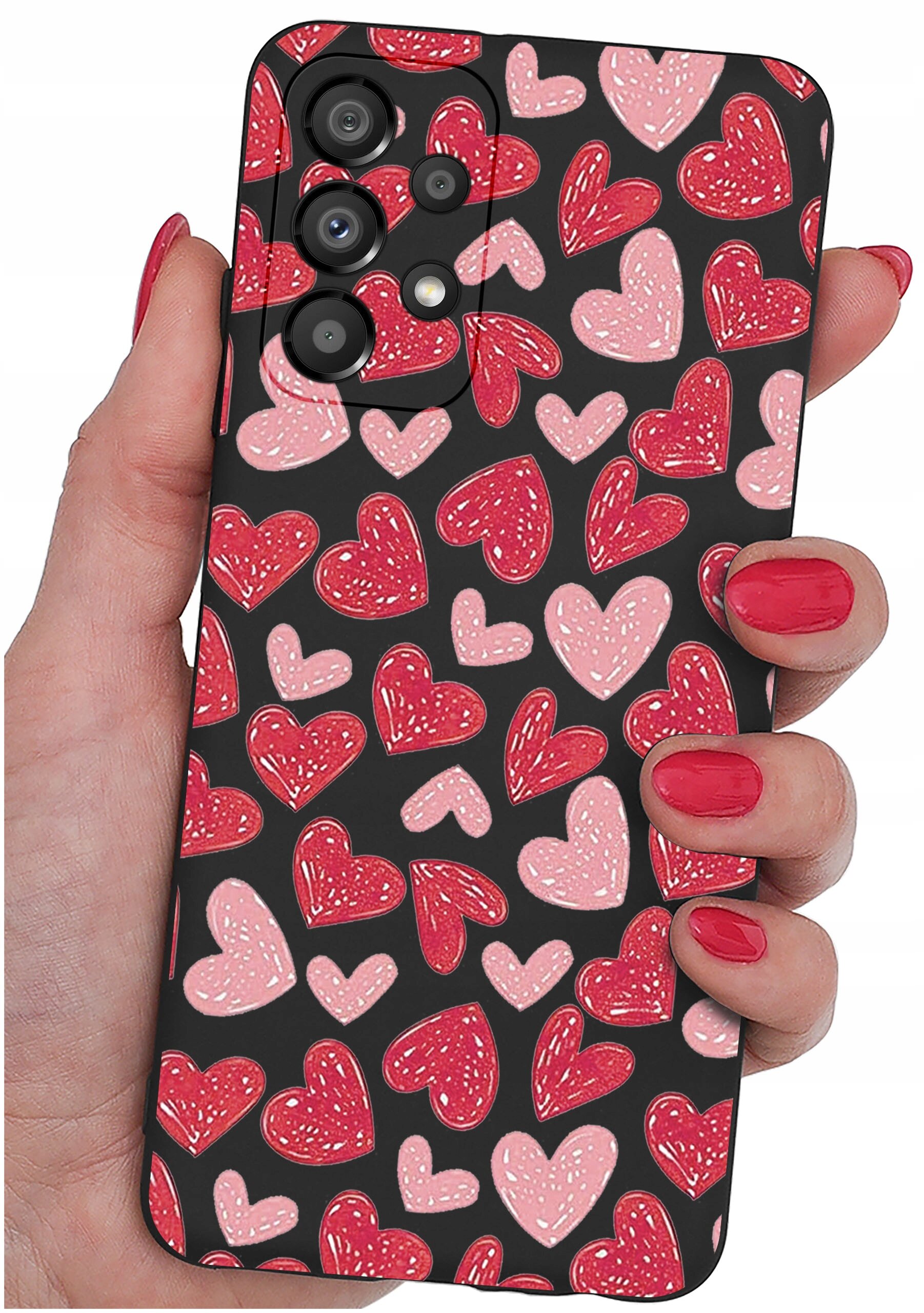 Etui na telefon z wzorem czerwonych i różowych serc trzymane w dłoni z pomalowanymi na czerwono paznokciami. Etui ma trzy otwory na aparaty fotograficzne.